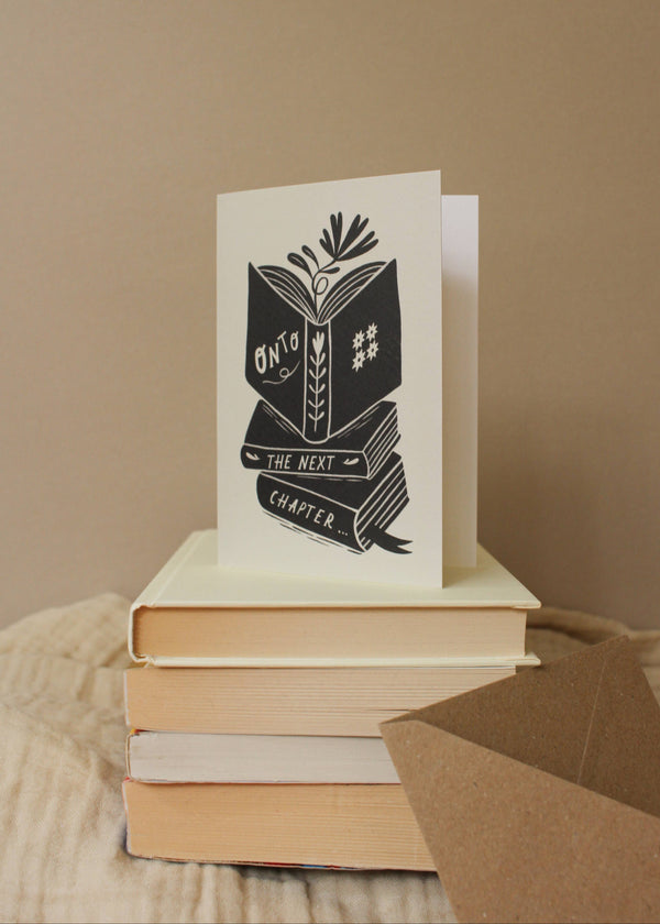 Stack of books with a card on top featuring a design and text.