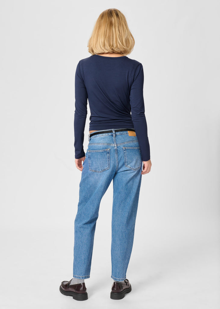 Person wearing a navy long-sleeve top and blue jeans on a white background