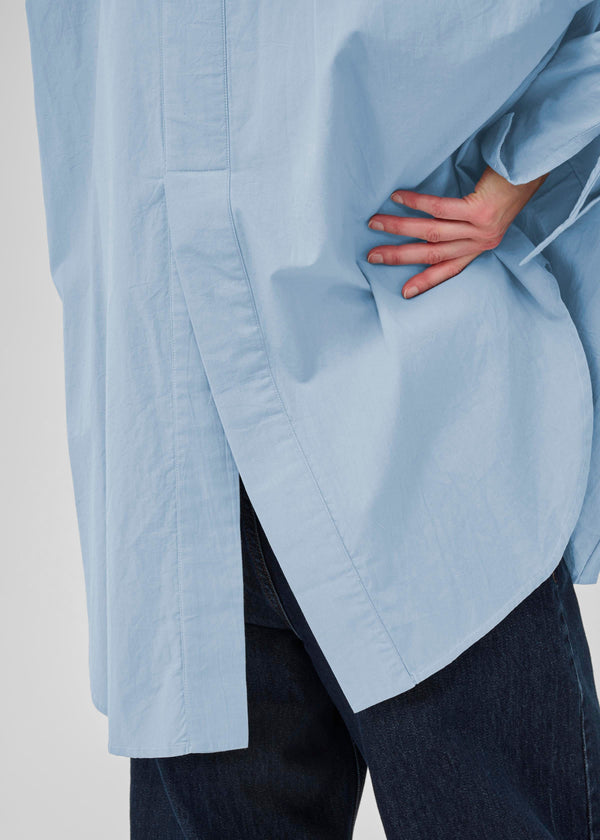 Light blue oversized shirt worn over dark jeans on a plain background