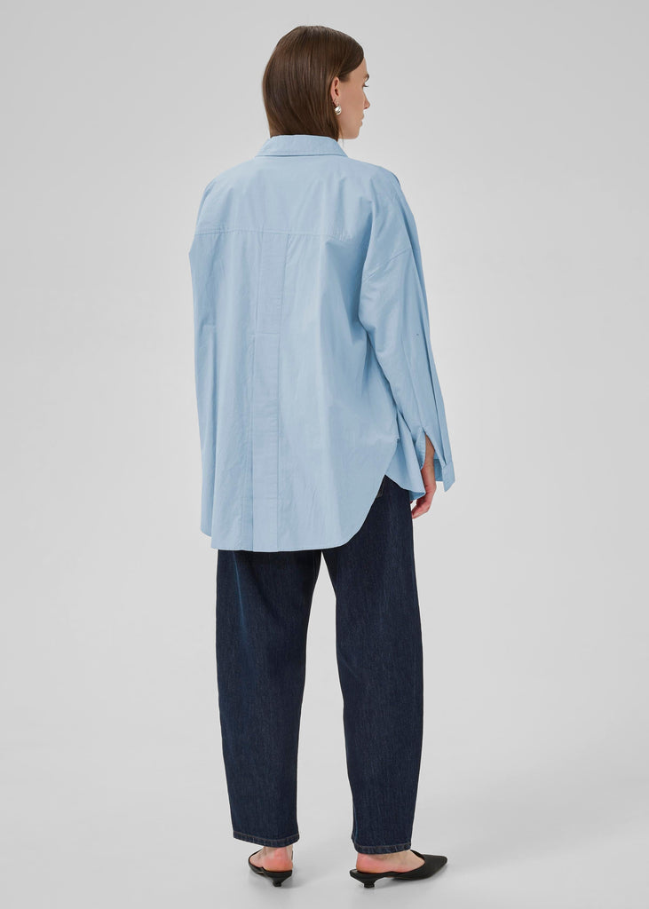 Person wearing a light blue striped shirt and dark pants on a white background