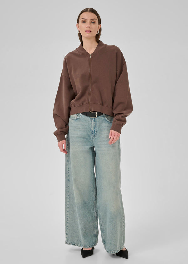 Person wearing a brown sweater and light blue jeans on a white background