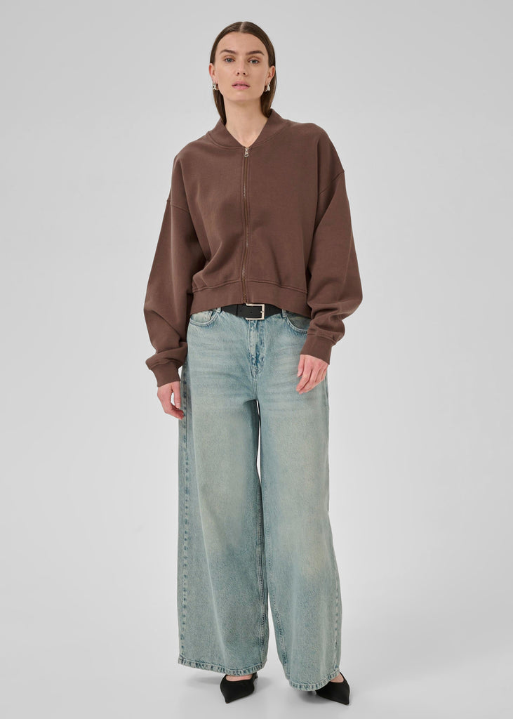 Person wearing a brown sweater and light blue jeans on a white background