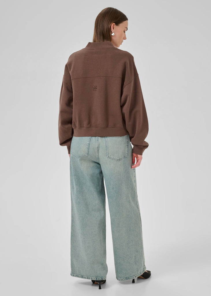 Person wearing a brown jacket and light blue jeans on a white background