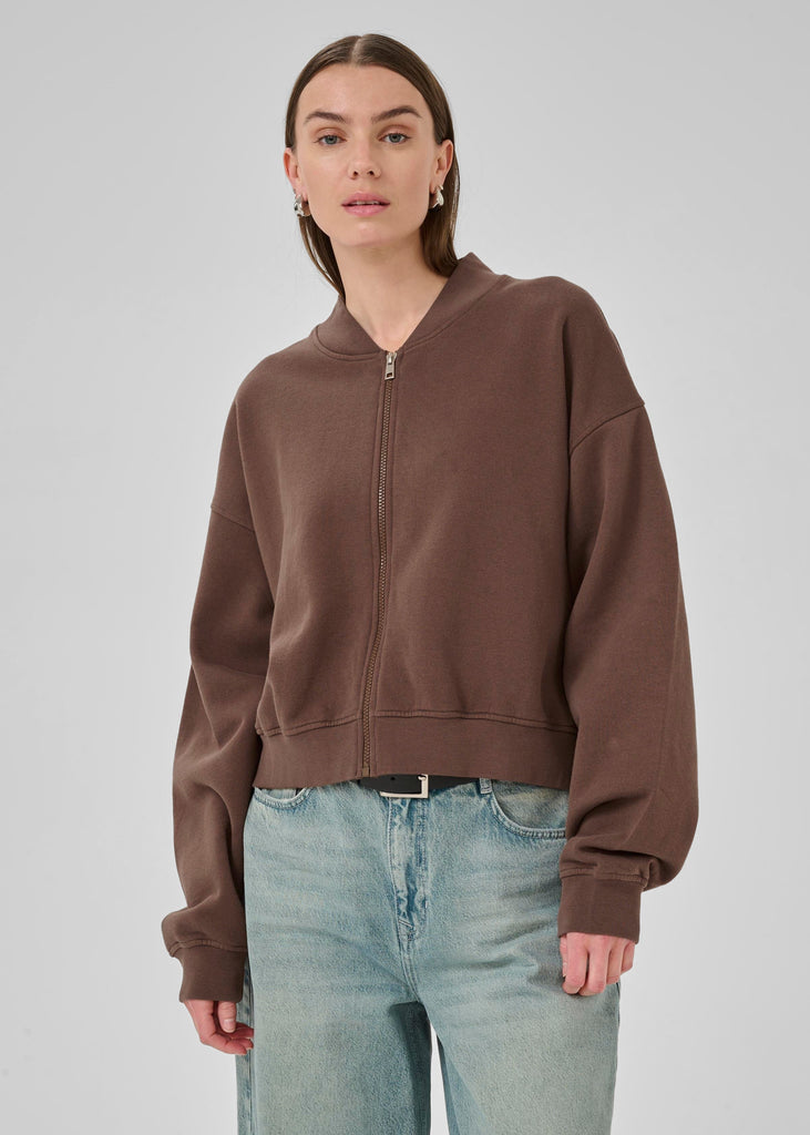 Woman wearing a brown zip-up hoodie and light blue jeans on a white background