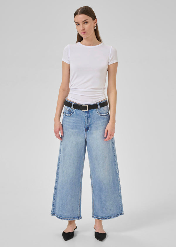 Woman wearing a white t-shirt and light blue jeans on a plain background