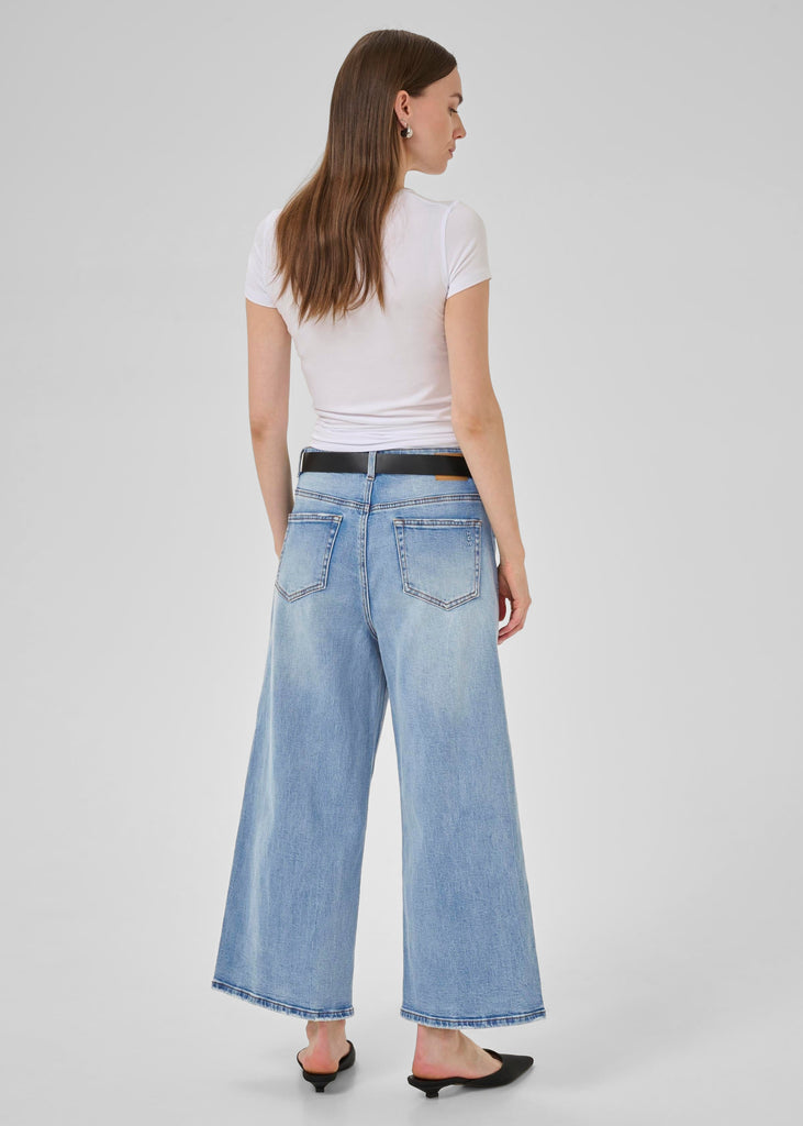 Woman wearing a white t-shirt and light blue jeans on a plain background