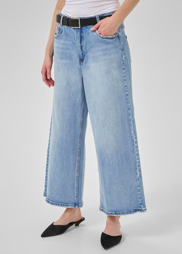 Person wearing light blue jeans and a white top on a plain background