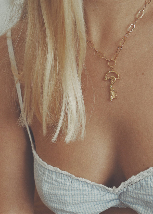 Gold necklace with a key pendant worn by a person with blonde hair.