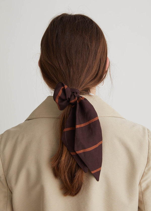 Person wearing a brown striped hair scarf in a ponytail against a plain background
