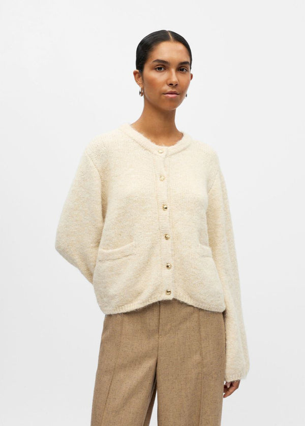 Woman wearing a cream cardigan and beige pants on a white background