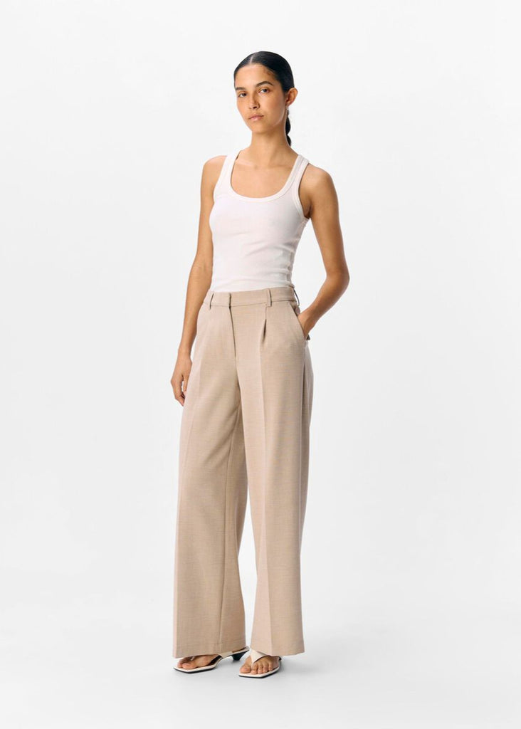 Woman wearing a white tank top and beige high-waisted pants on a white background