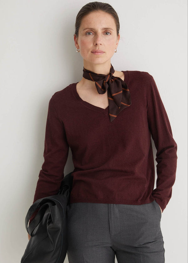 Woman wearing a burgundy sweater with a scarf, standing against a plain background