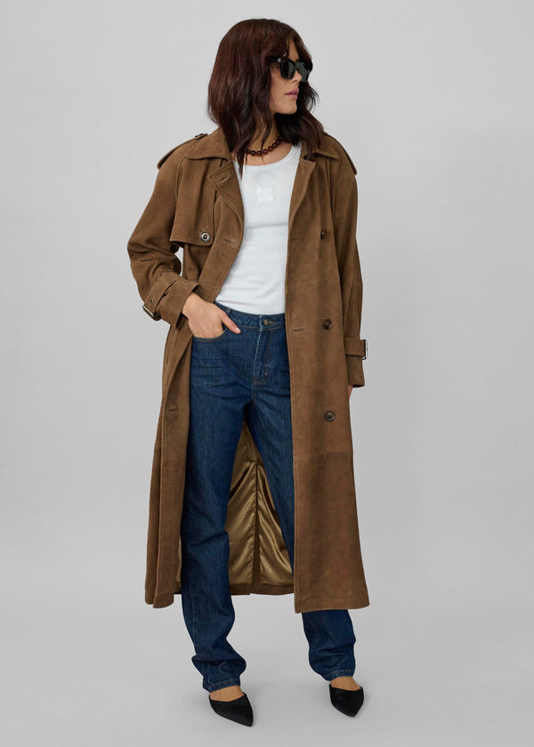 Woman wearing a long brown coat, white shirt, and blue jeans on a plain background