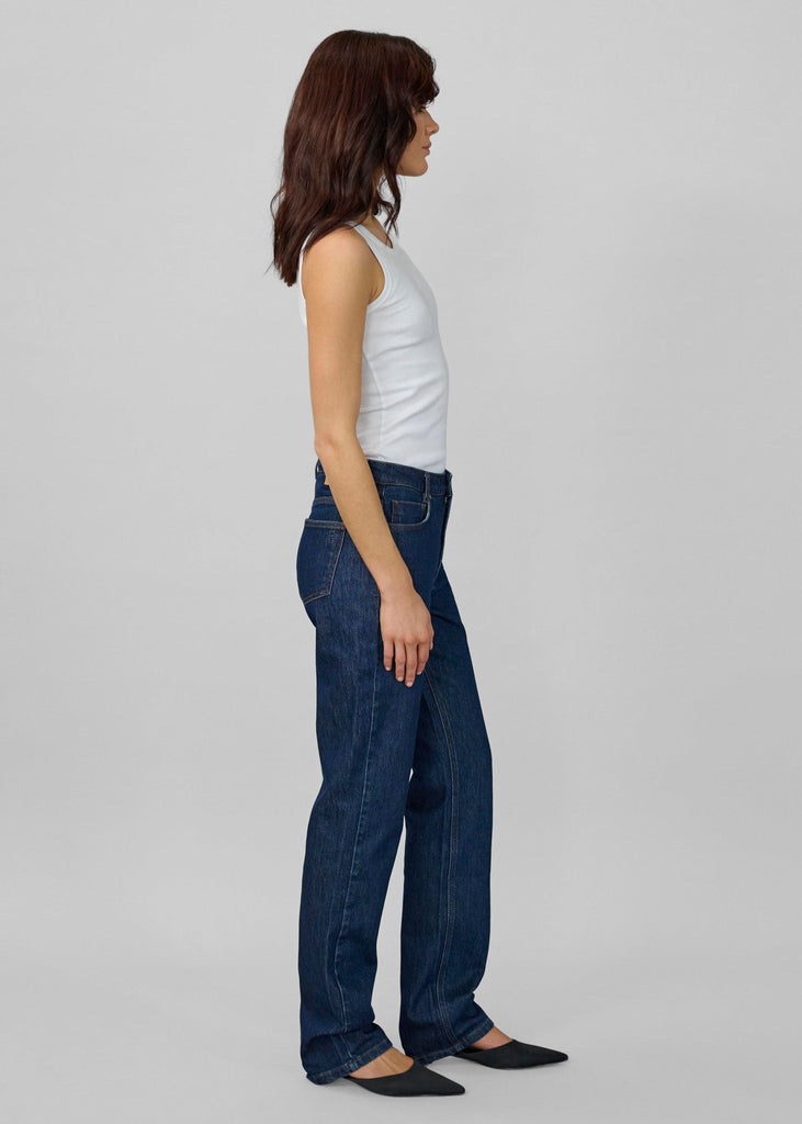 Woman wearing blue jeans and a white top on a plain background