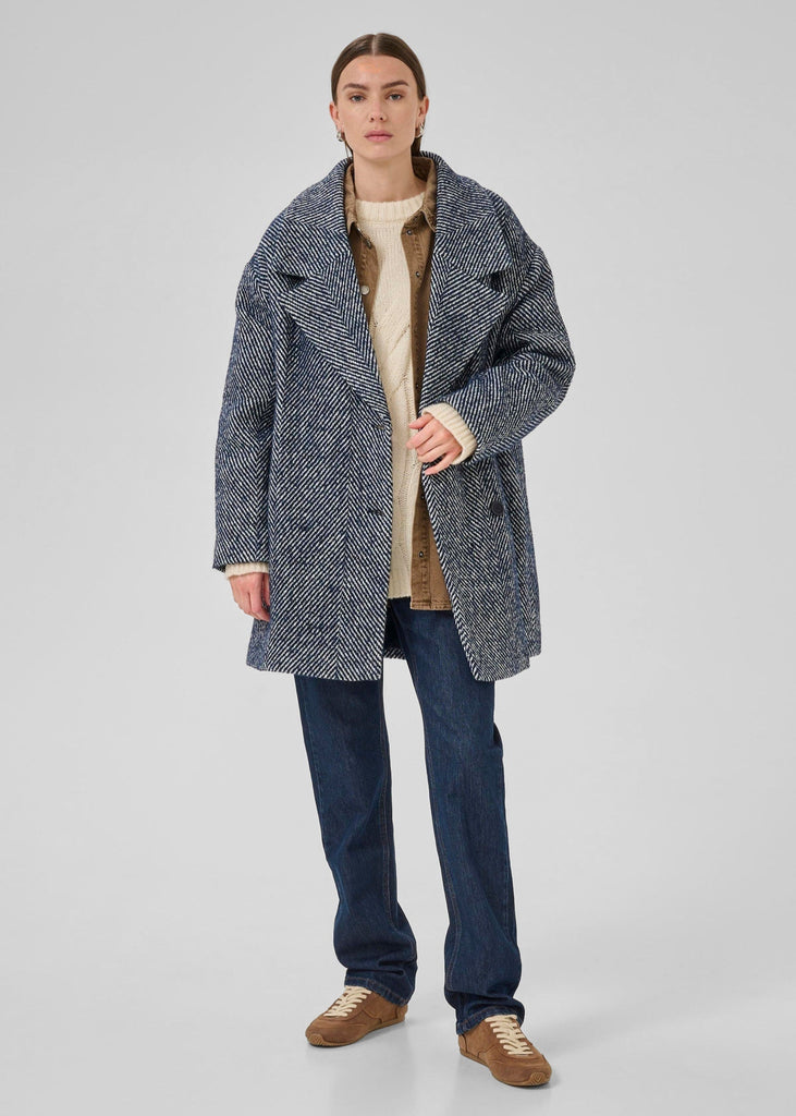 Person wearing a gray coat, beige sweater, blue jeans, and brown shoes on a white background