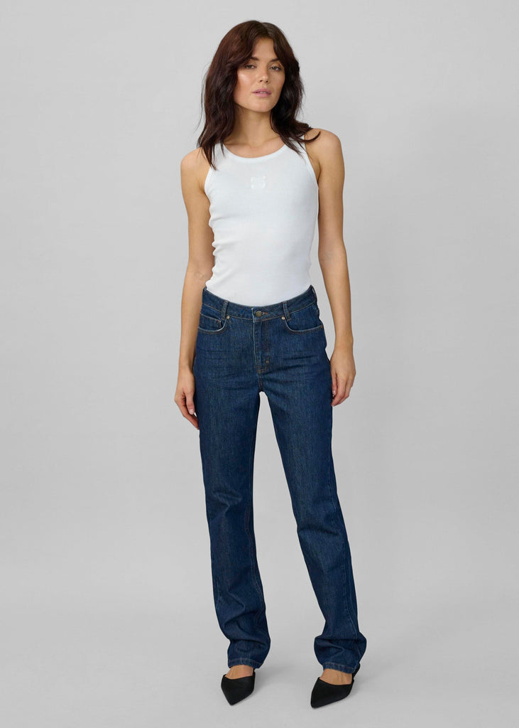 Woman wearing a white tank top and blue jeans on a gray background