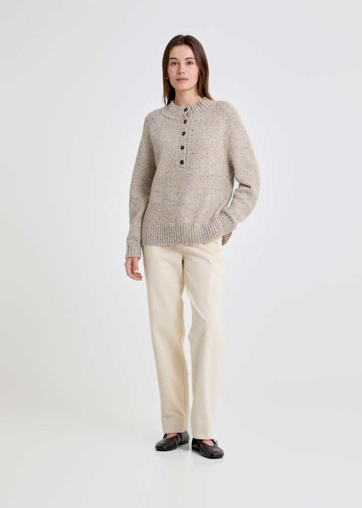 Woman wearing a beige sweater and cream pants on a white background
