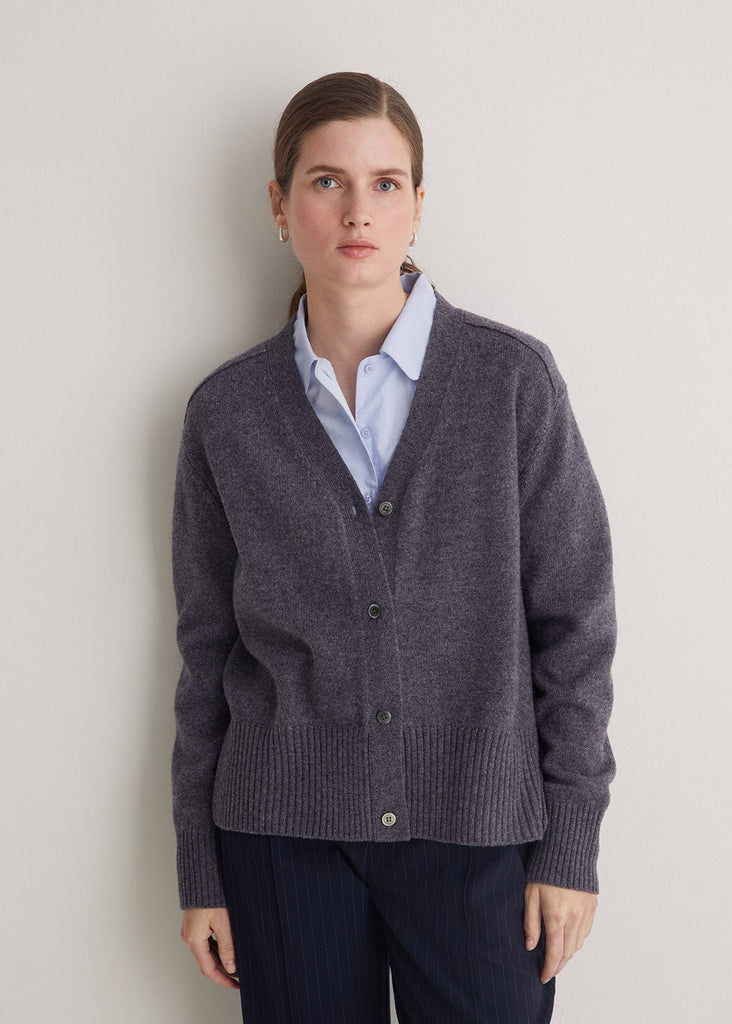 Woman wearing a gray cardigan over a light blue shirt against a plain background