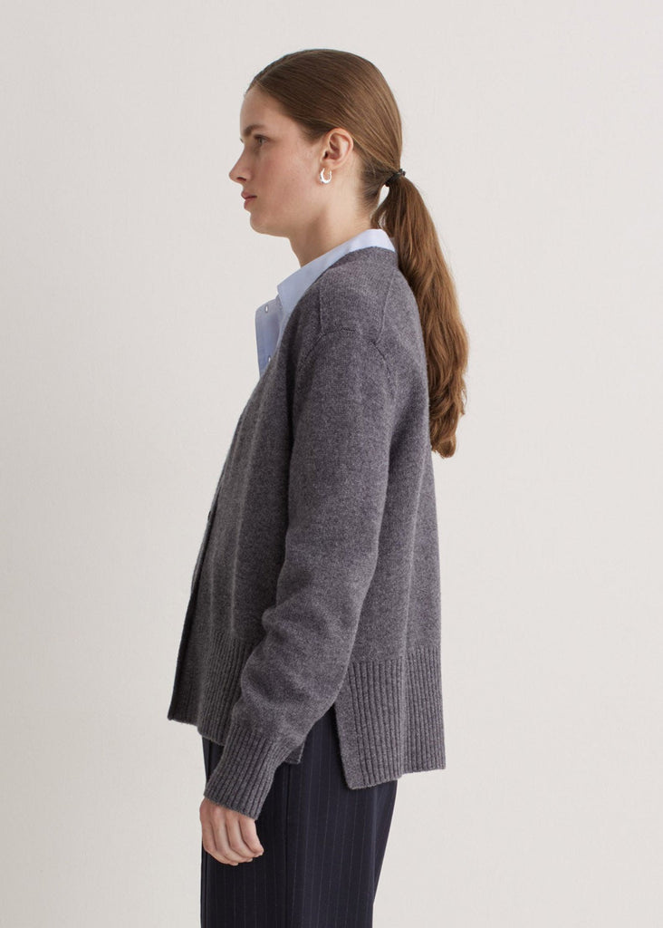 Woman wearing a gray cardigan over a light blue shirt on a plain background