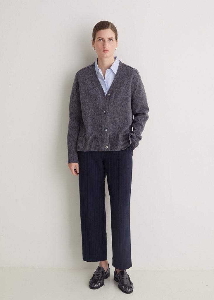 Person wearing a gray sweater, white shirt, and dark pants on a plain background