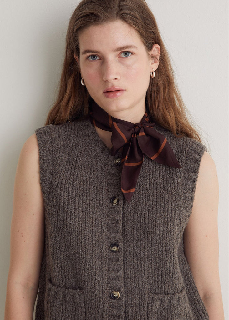 Woman wearing a brown ribbed vest and scarf against a plain background