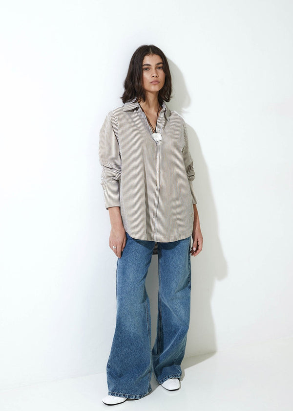 Woman wearing a beige button-up shirt and blue jeans against a white background