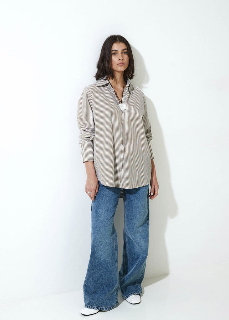 Woman wearing a beige button-up shirt and blue jeans against a white background