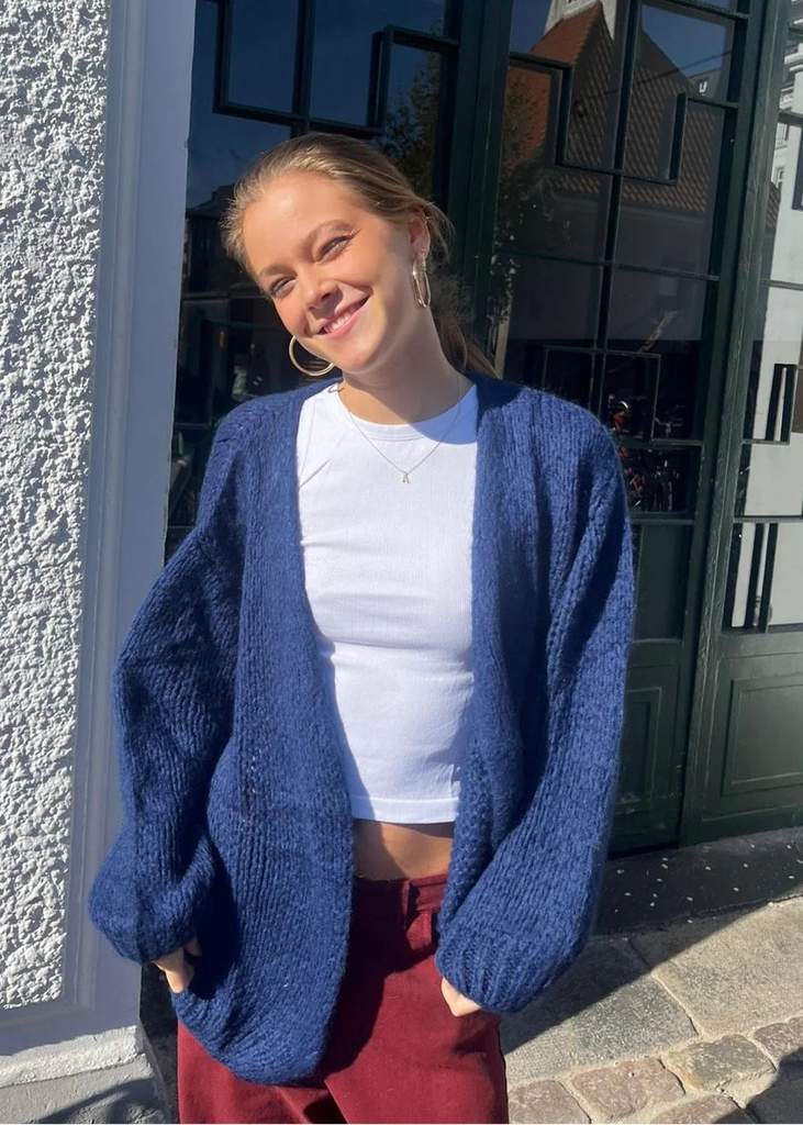 Woman wearing a blue cardigan and white top standing outside a building.
