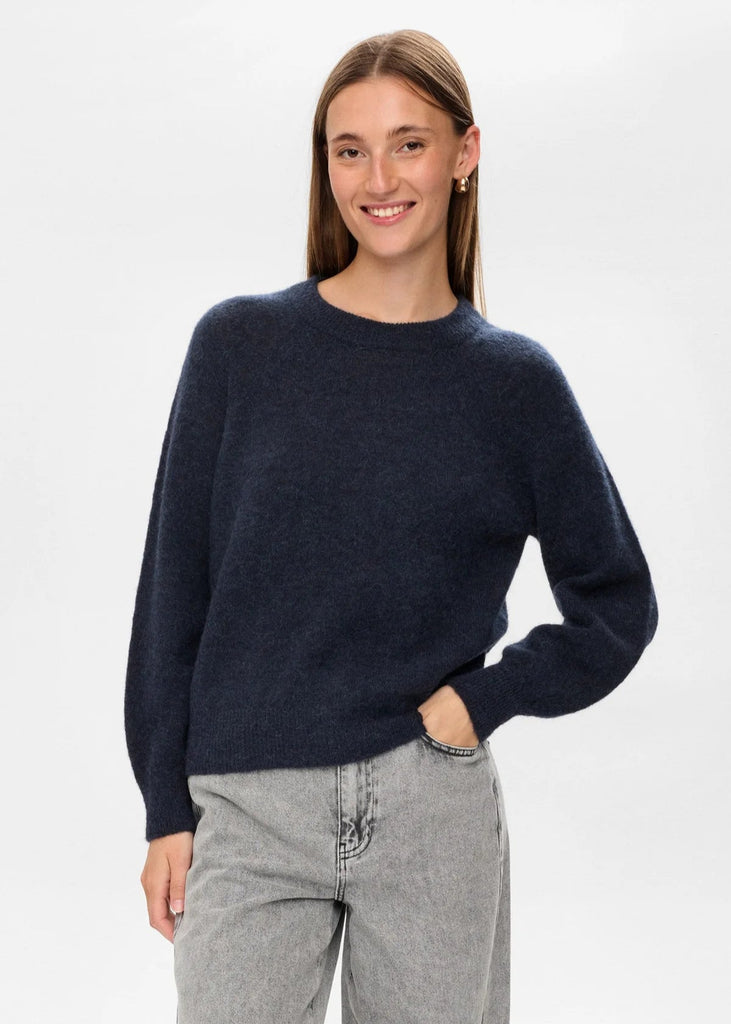 Woman wearing a navy sweater and gray pants on a white background