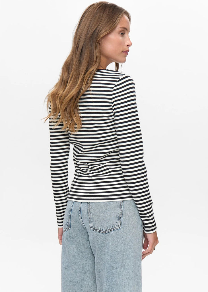 Woman wearing a black and white striped long-sleeve top with light blue jeans on a plain background