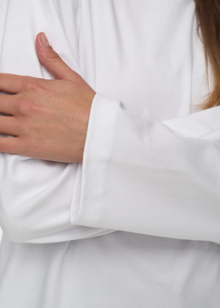 Close-up of a person wearing a white robe with a hand on the chest.