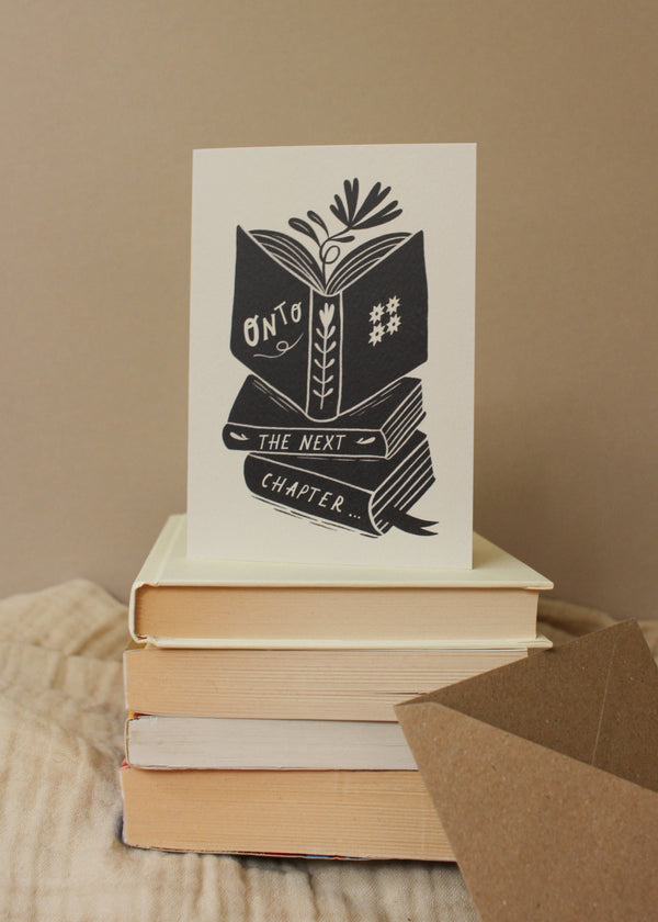 Stack of books with a card reading 'Open the next chapter' on a wooden surface.