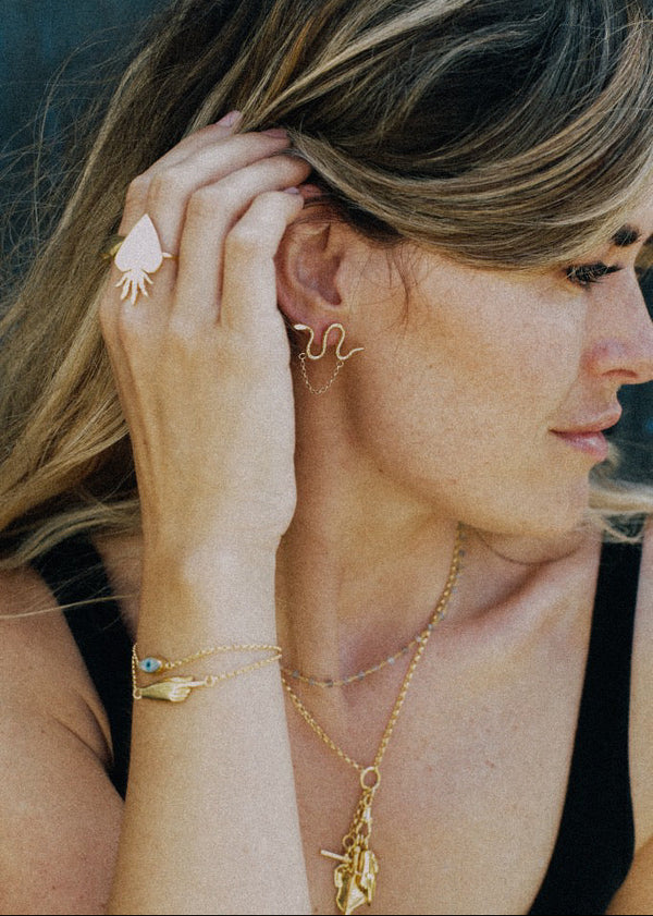 Woman wearing gold jewelry including earrings, necklace, and ring.