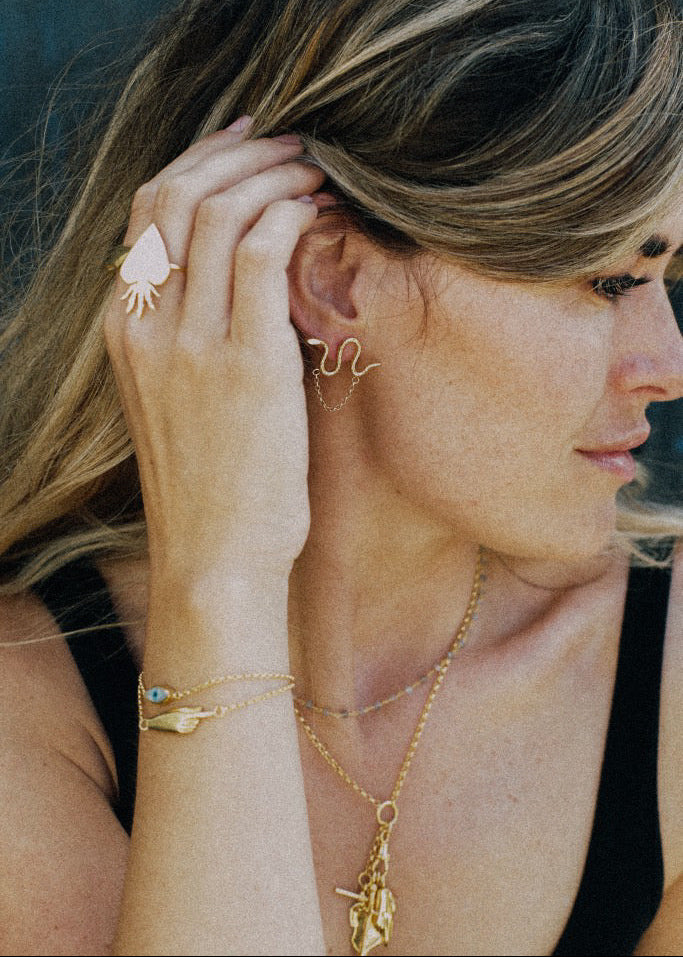 Woman wearing gold jewelry including earrings, necklace, and ring.