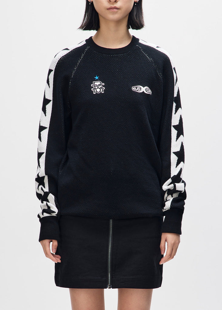 Person wearing a black sweater with white patterns and small logos on a light gray background