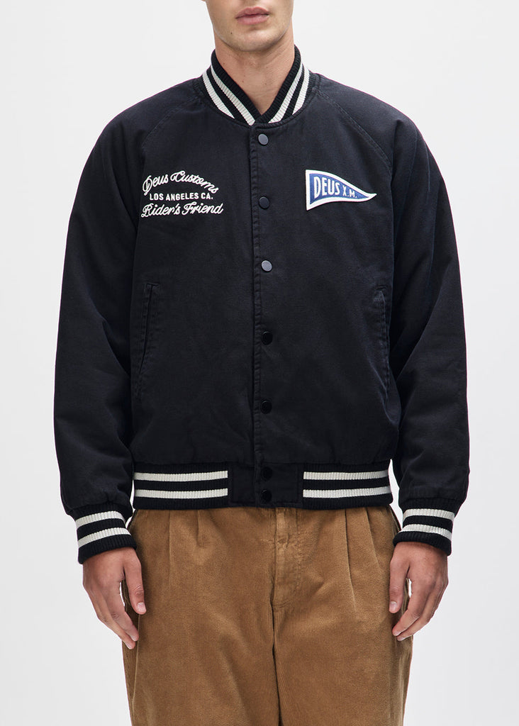 Person wearing a black varsity jacket with white lettering and trim on a light gray background