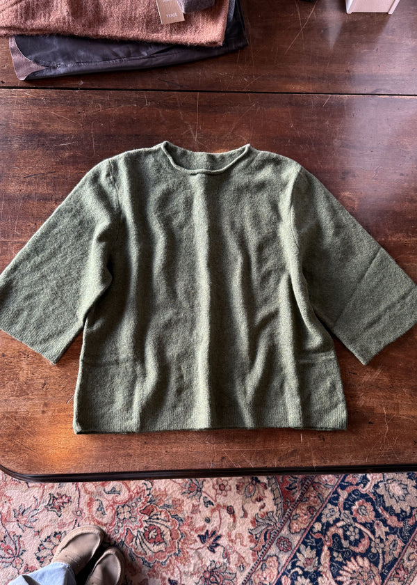 Green sweater on a wooden table with a patterned rug underneath