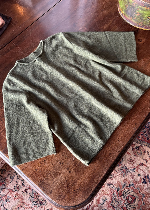 Green sweater on a wooden surface with a patterned rug underneath