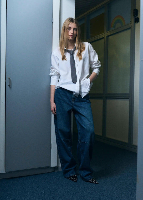Person wearing a white shirt and blue pants standing in a room with a gray door and colorful wall.