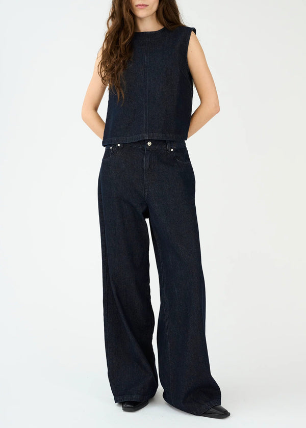 Woman wearing a black sleeveless top and wide-leg jeans on a white background