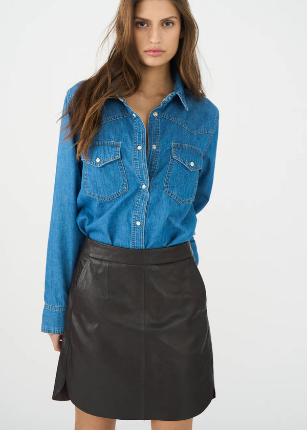 Woman wearing a blue denim shirt and black leather skirt on a white background