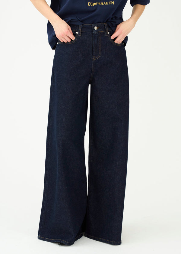 Person wearing dark blue wide-leg jeans and a navy shirt with a logo on a white background