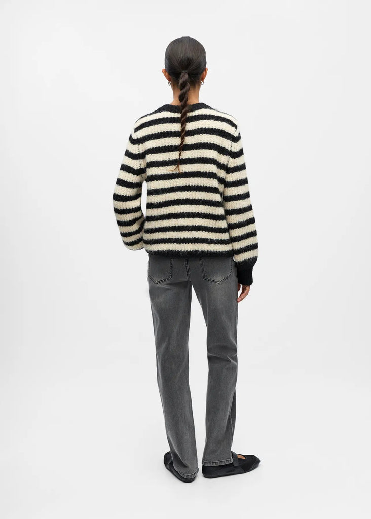 Person wearing a black and white striped sweater and gray pants on a white background