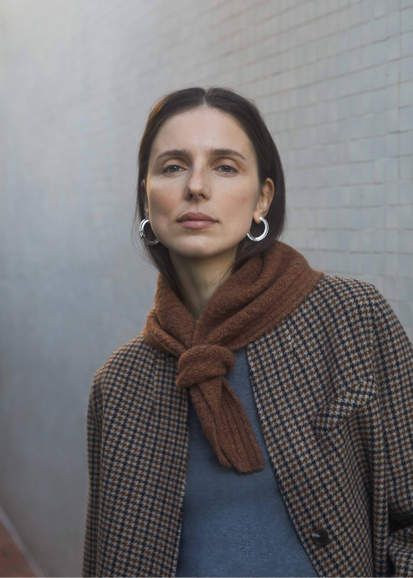 Woman wearing a brown scarf and checkered coat against a light gray wall