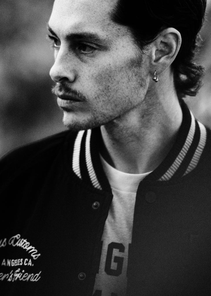 Black and white portrait of a person wearing a varsity jacket with visible branding.