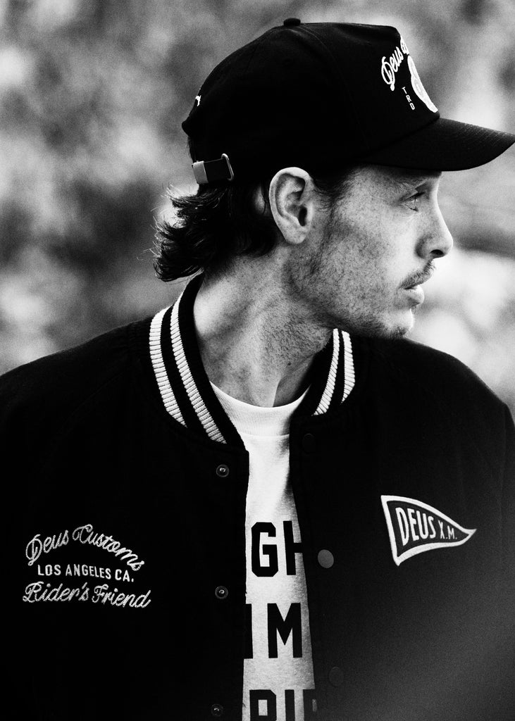 Person wearing a black varsity jacket with visible branding, standing outdoors.