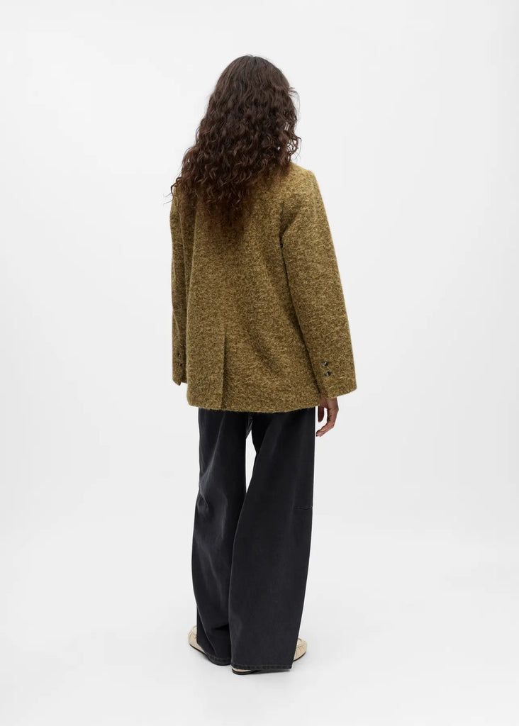 Person wearing a green textured jacket and black pants on a white background