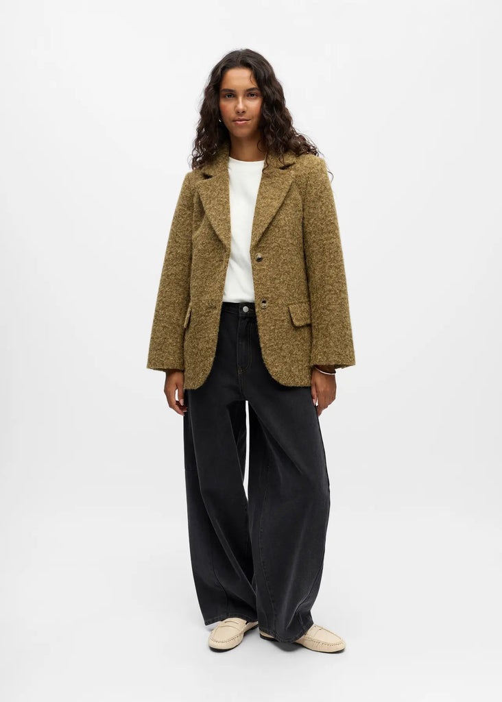 Woman wearing a green blazer over a white shirt with black pants on a white background