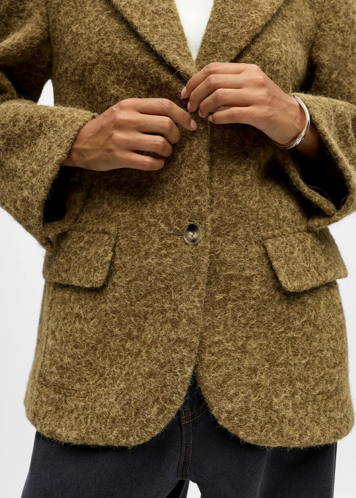 Person wearing a brown blazer with a white background