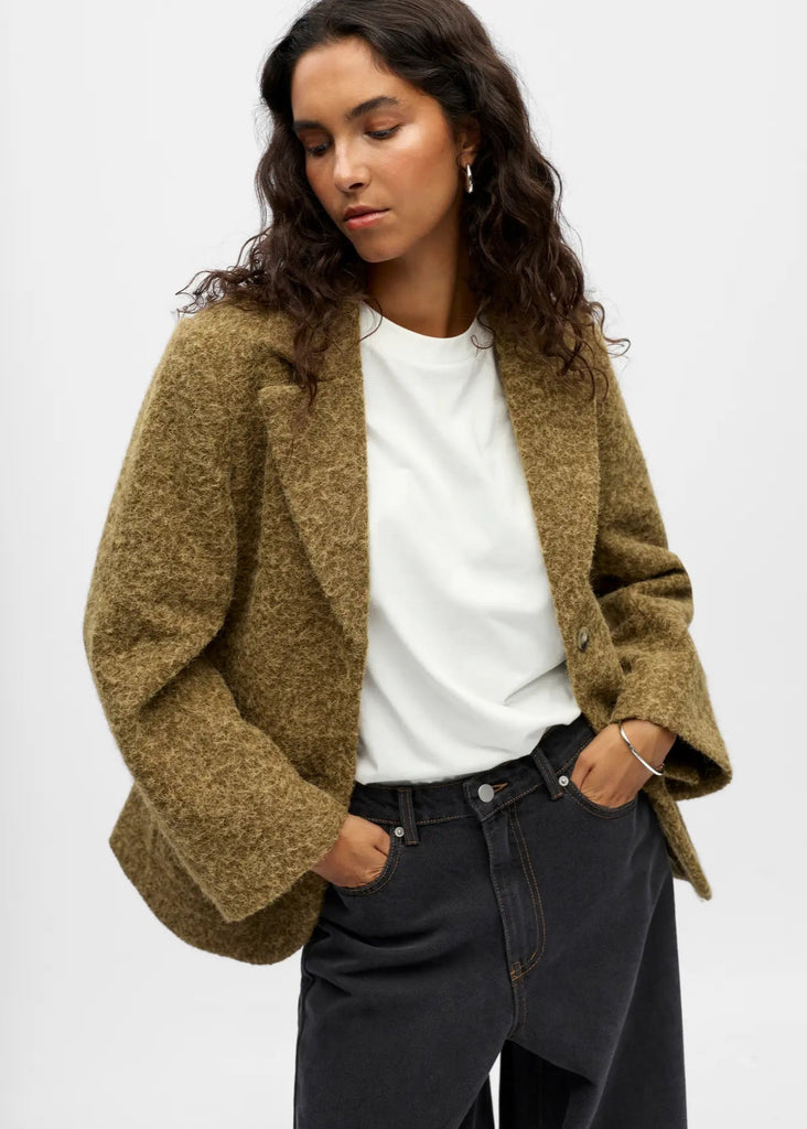 Woman wearing a brown cardigan over a white shirt and black pants on a white background